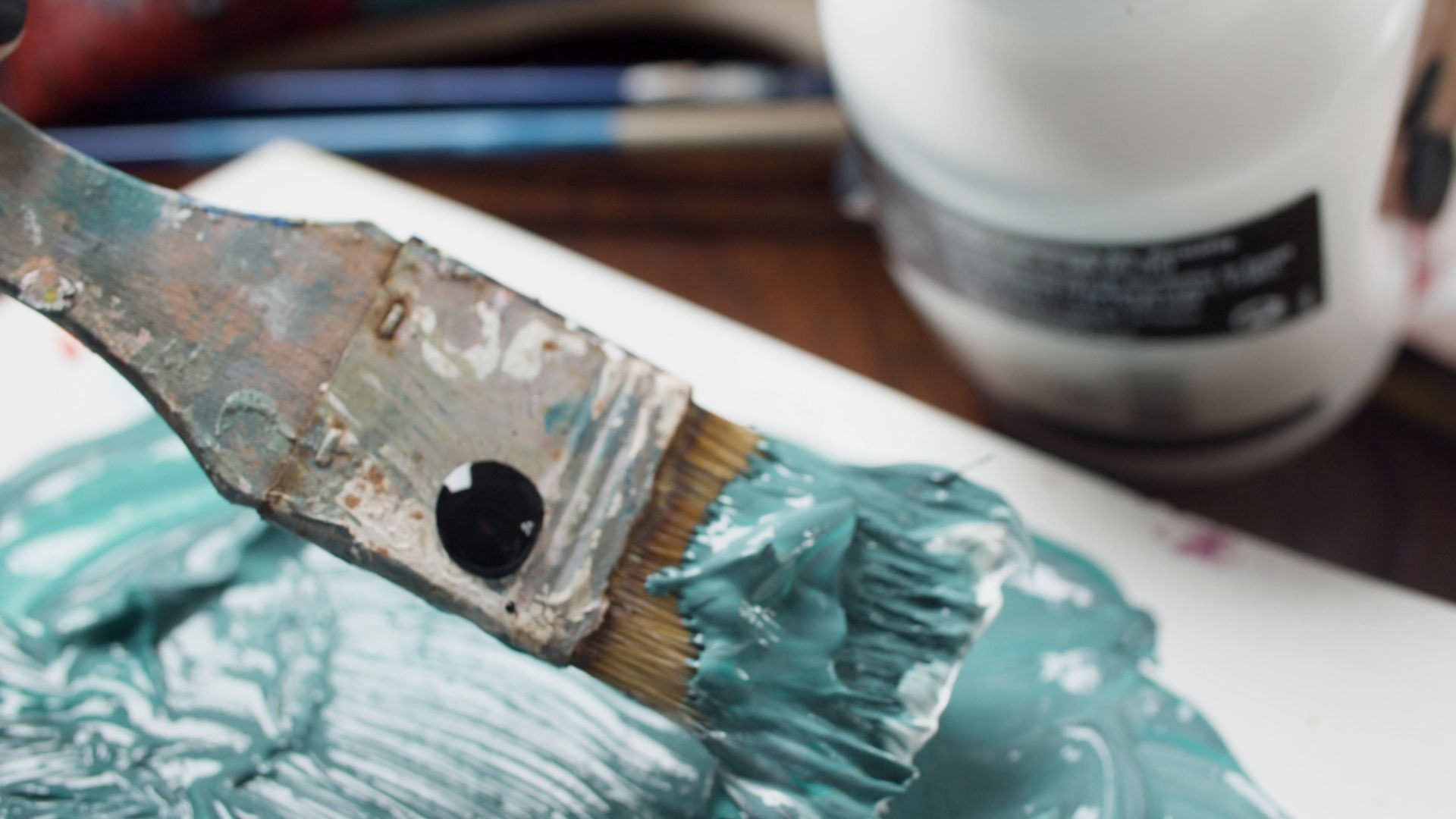 A palette knife spreading thick teal paint